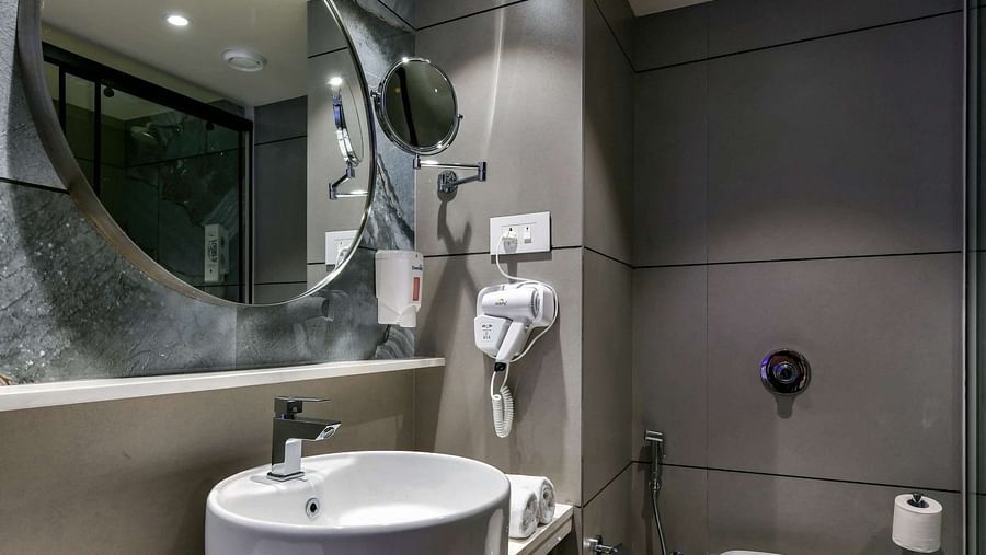A washroom featuring a washbasin with a wall-mounted mirror above and a western toilet, at Indie Stays, BKC Kalina.