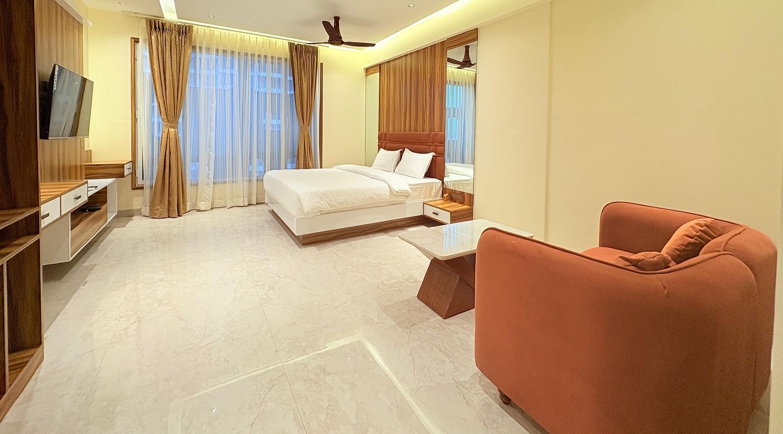 Side view of a bedroom featuring a large cushioned sofa, ceiling fan, and wall-mounted television at Hotel Mumbai House, Vashi.