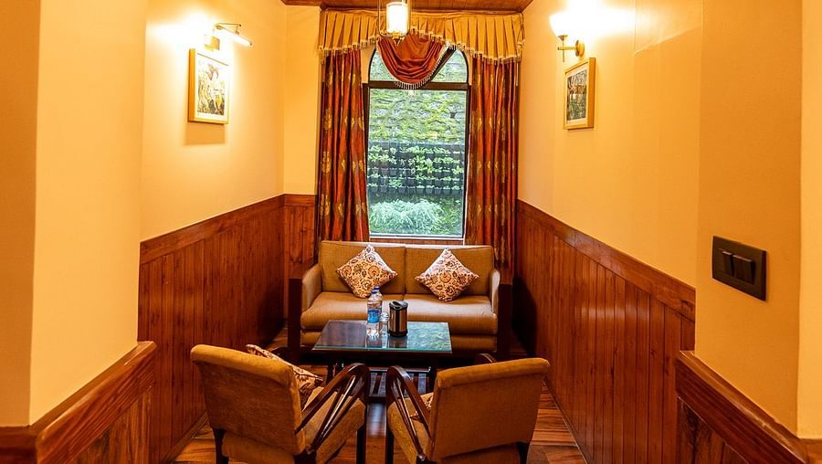 A warm, inviting hallway of Oak Room with an arched ceiling and wood panelling leads to a cosy seating area at The Pavilion, Nainital