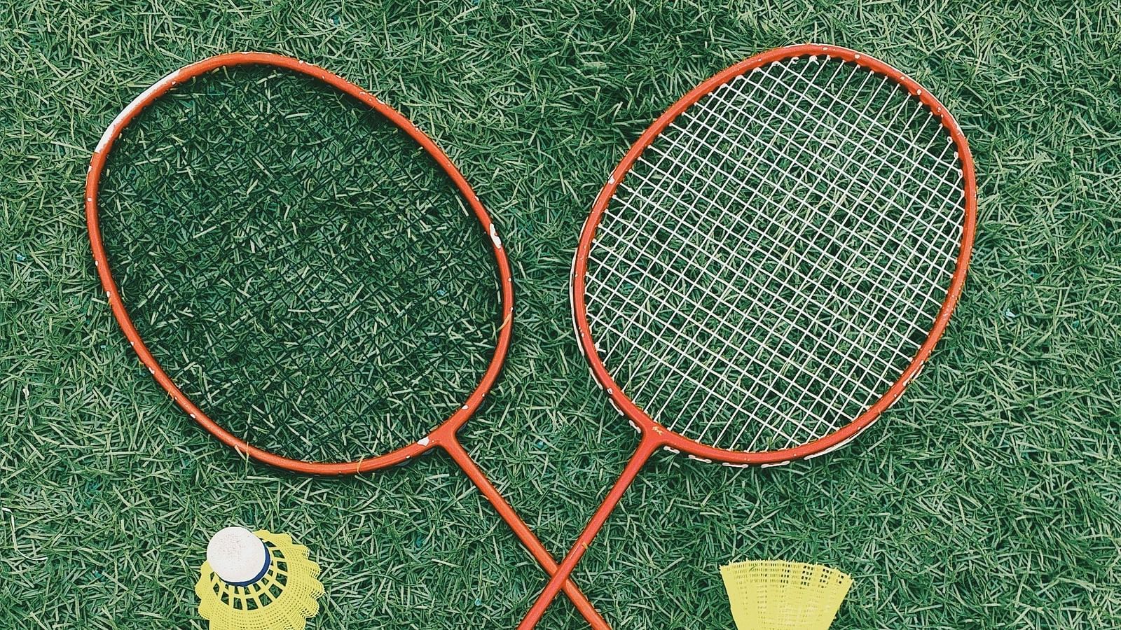 Top view of two badminton raquets, two shuttles and a water bottle on a grass surface.