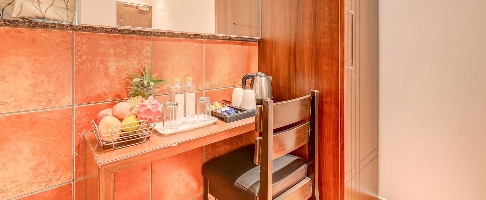 A wooden desk at Harigovinda's JNStay with a wooden chair, fruits, glasses, and a kettle placed on it