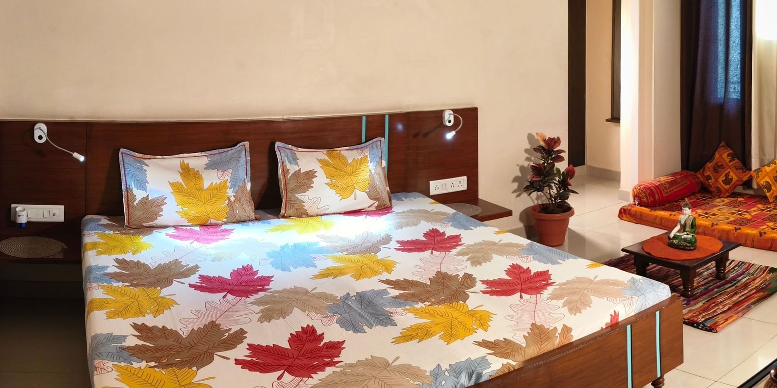 A spacious bedroom with a double bed, colourful bedding, a sofa set and a wall painting above the bed at Jaypore360 Homestay - Best Homestays in Jaipur.