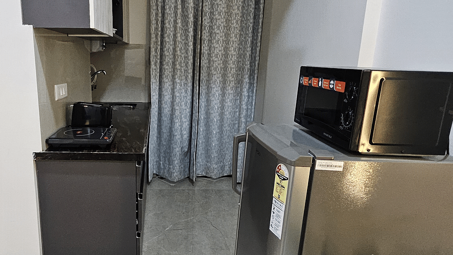 Compact kitchenette in a studio room featuring a refrigerator, microwave, induction cooktop, sink, and overhead cabinets with a curtain partition - Urban Suites by BluSalzz, Jaipur