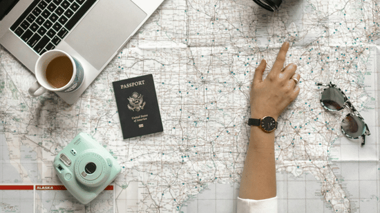 A top-down view of a person’s arm over a paper map surrounded by a laptop, camera, and passport | HHI Varanasi