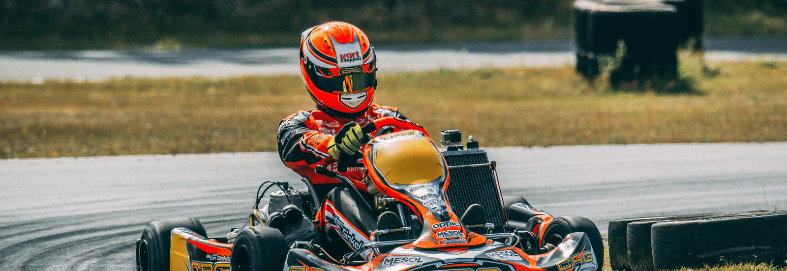 A racer in a helmet is driving a small go-kart on an outdoor race track.