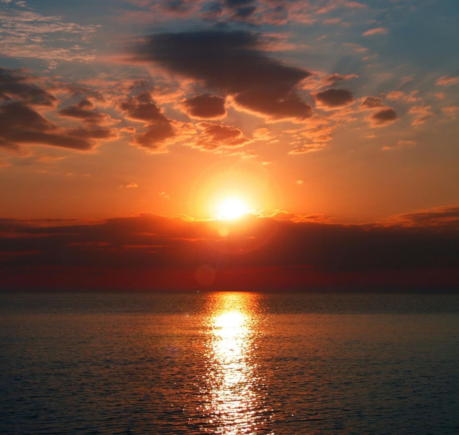 A beautiful sunset with the sun rays reflecting on the ocean bed along with a cloudy sky in the background.