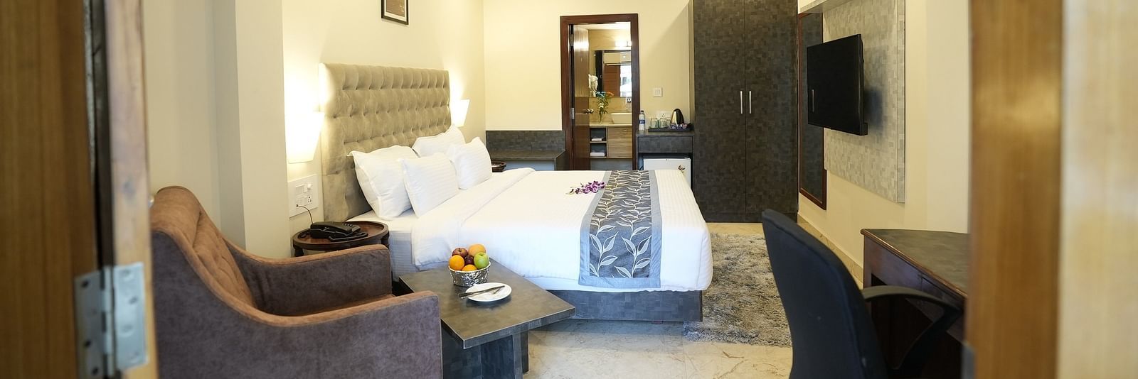 A well-lit modern bedroom with twin beds, a plush armchair, and a wall-mounted TV – The Verda de Miranda Resort.