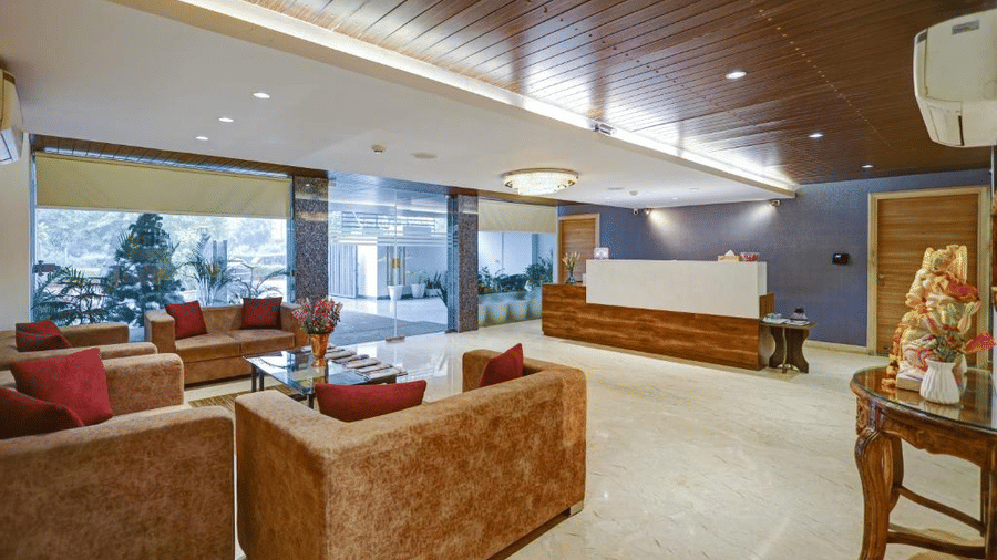 The reception area at Hotel 91 HUDA Premier, Gurugram with sofas, chairs, tables, wooden ceiling, large windows, and a reception desk in the background.