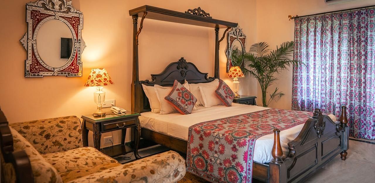 A Deluxe Room with a four-poster bed, a window, a sofa, and elegant decor with warm lighting - Khas Bagh, Jaipur