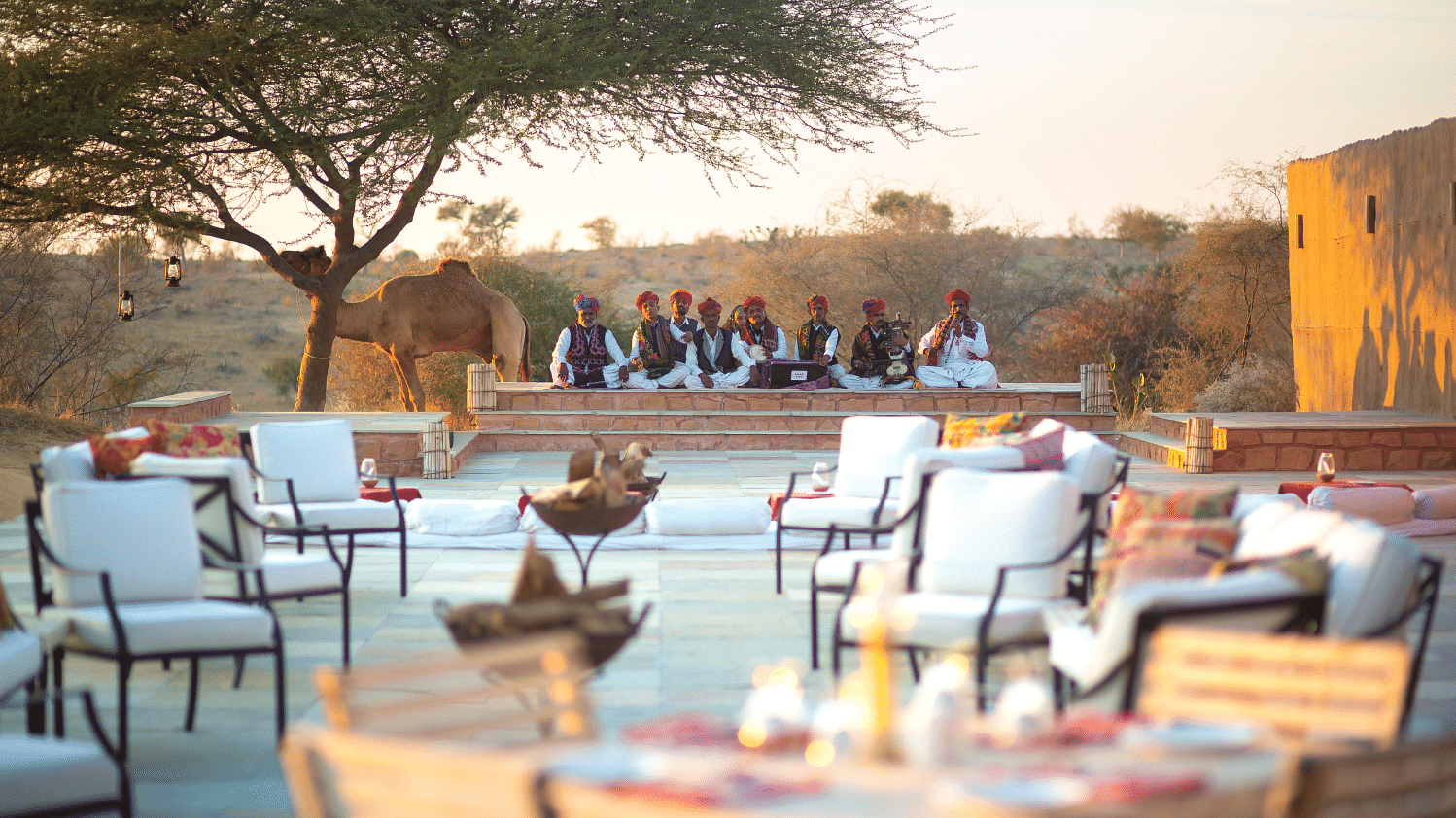 An image of outdoor seating area with seating arrangement placed in front of a podium where a group of men are sitting wearing traditional Rajasthani outfit - MANVAR Resort & Desert Camp