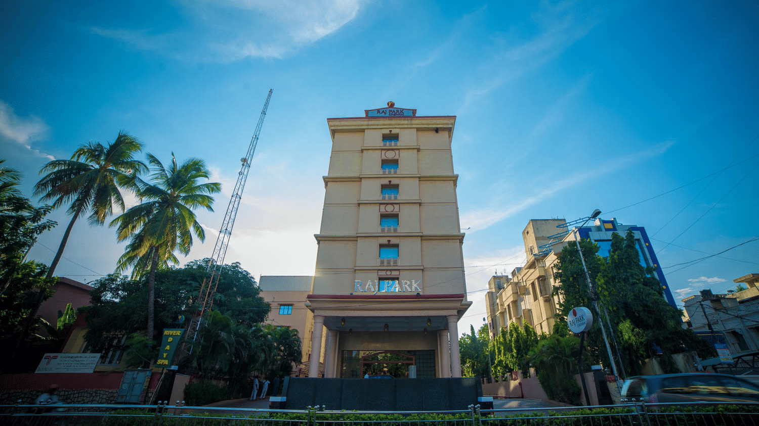 Facade view of Raj Park Hotel in Alwarpet with blue sky in the background.