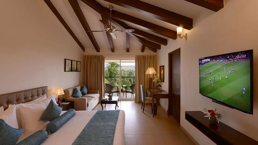A wide angle view of a hotel room in Candolim featuring a king size bed, high ceilings, modern amenities, and a balcony with lush green views - Golden Tulip, Candolim, Goa