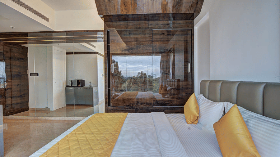 A double bed with pillows and cushions placed over it with a huge glass panel mirroring the city views from the exterior in the Grand Suite at SRS Suites, Koramangala.