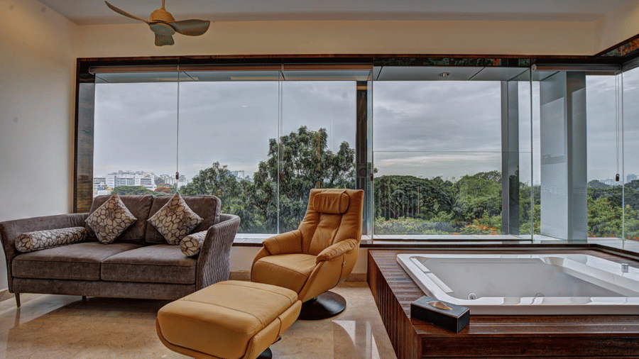 The Grand Suite featuring a a Jacuzzi tub along with a couch and an arm chair in the living room of the Grand Suite overlooking the city views from the window at SRS Suites, Koramangala.