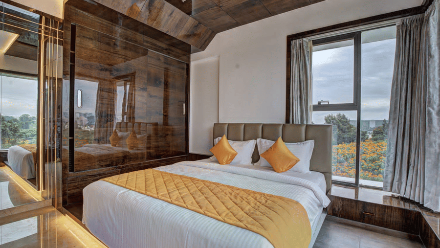 Full view of the double bed at the Grand Suite with a yellow-coloured bed runner spread over it overlooking the beautiful city views from the window beside it at SRS Suites, Koramangala.