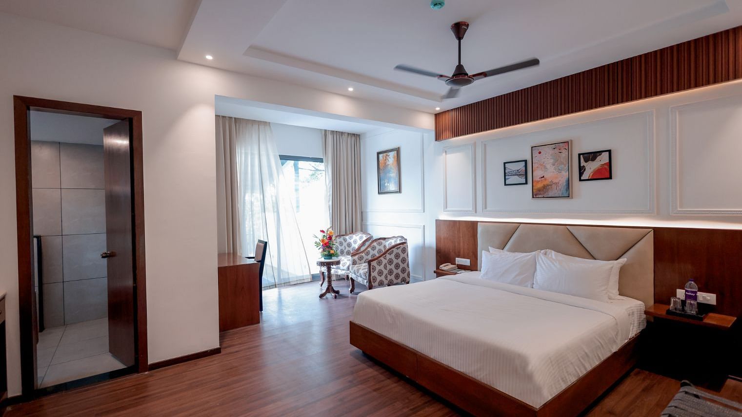 A bedroom with double bed, chair, round table and framed art work at Trishvam Symphony, Krishnagiri