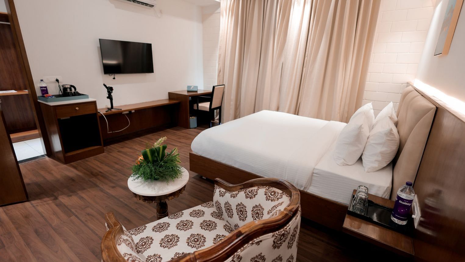 A bedroom with double bed, table, desk, TV and a framed art work at Trishvam Symphony, Krishnagiri