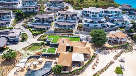 An aerial view of a luxury resort complex with multiple buildings, pools, and lush landscaping, situated near a coastline.