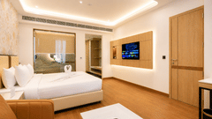 Suite bedroom view featuring a double bed, a wall-mounted television, wooden flooring, and a doorway at Pride Premier Greater Noida.