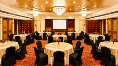 Banquet hall at Pride Premier Pune with round tables, black chair covers and a chandelier ceiling.
