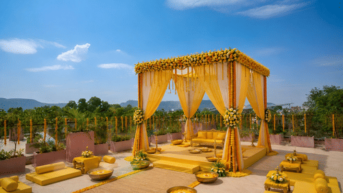 An outdoor event setup featuring a canopy structure on a platform with floor seating cushions and bolsters around it.