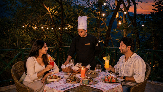 A chef serving drinks and food to a couple on a illuminated terrace at Neemrana's Glasshouse on The Ganges - 21st Century, Rishikesh.