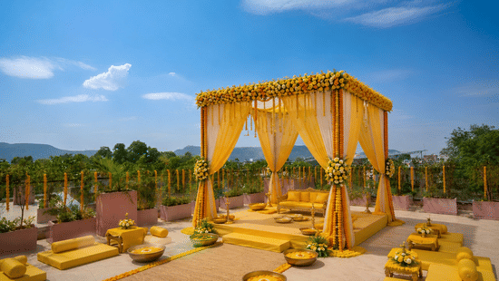 An outdoor event setup featuring a canopy structure on a platform with floor seating cushions and bolsters around it.