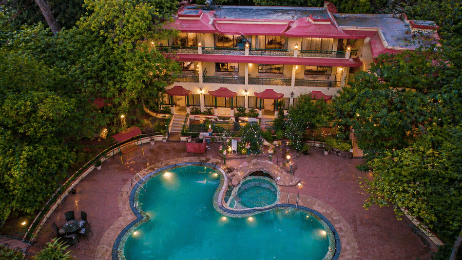 An aerial view of the hotel swimming pool and the hotel building surrounded by lush green trees.