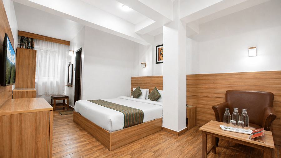 A Heritage Deluxe Non View room at Central Heritage Resort and Spa featuring a king bed with striped runner wooden wall panels hardwood flooring a wooden sofa and a wall-mounted TV on the side.