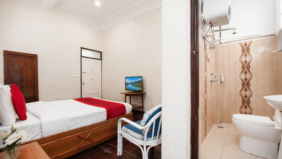 Split view of a room at Central Hotels showing a bedroom with red and white bedding wooden furniture and wall-mounted TV alongside an attached bathroom with shower toilet and tiled walls.