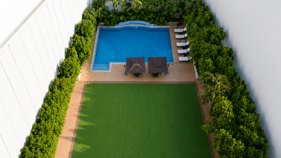 Aerial view of hotel pool courtyard with manicured lawn, sun loungers, and lush tree border.