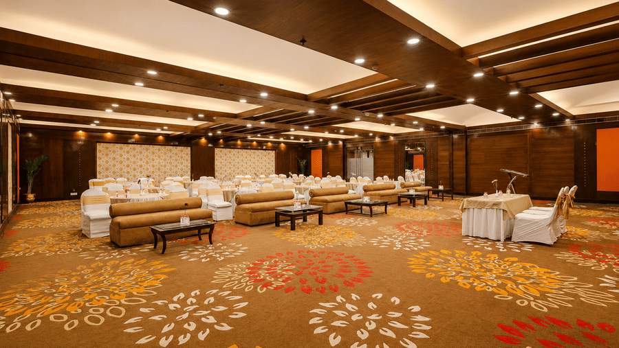 Spacious banquet hall with vibrant floral carpet, wood-panelled ceiling, and open seating arrangement