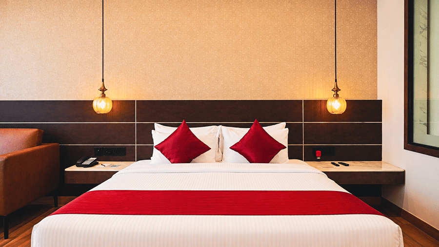 Spacious king-bedded guest room with warm lighting, wooden flooring and modern interiors at HM Hotel & Resort, Dibrugarh, offering a comfortable stay in Assam