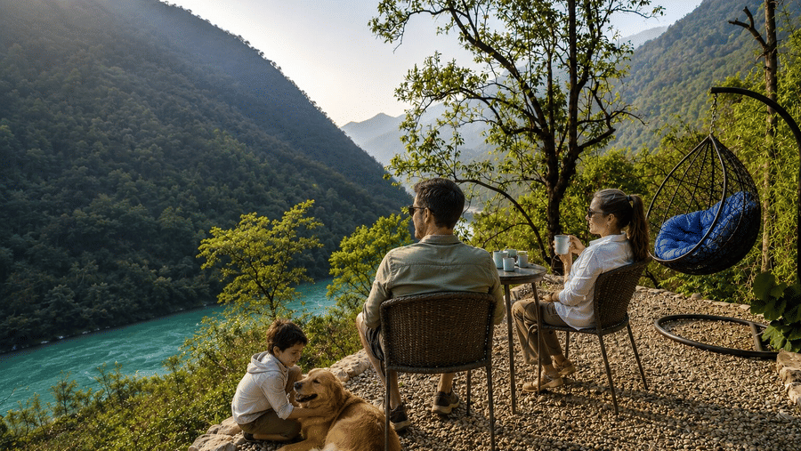 A family relaxing with their dog on a gravelled terrace overlooking the river at Neemrana's Glasshouse on The Ganges - 21st Century, Rishikesh.