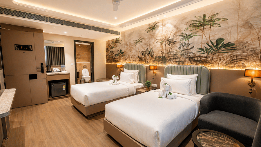 Pride Premier Alwar | A room with twin beds, bedspreads, pillows, windows covered with curtains.