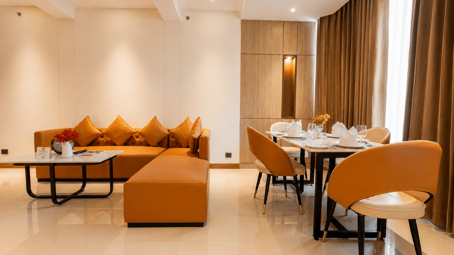 An open-plan Suite at Pride Premier Greater Noida, showing a living area with a sofa and coffee table alongside a dining table with chairs.