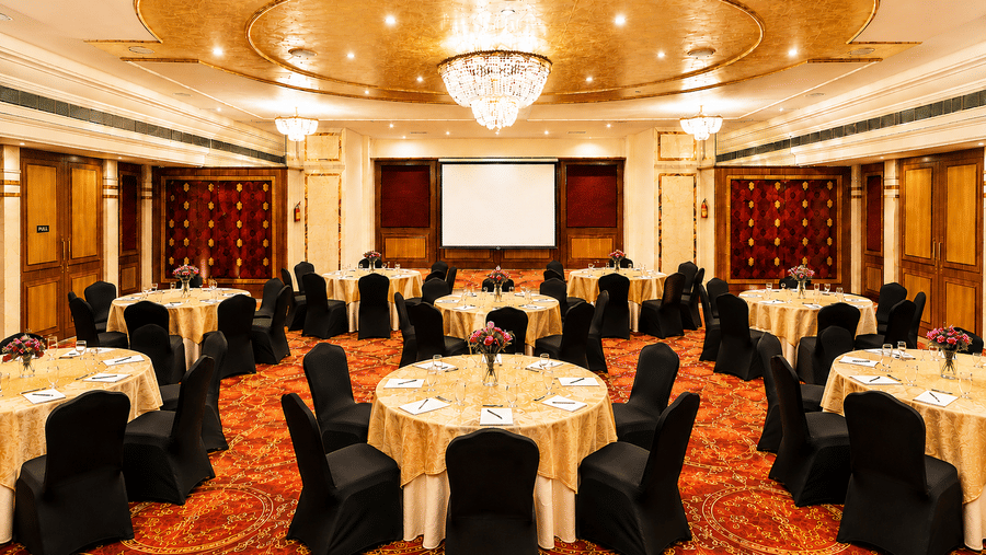 Banquet hall at Pride Premier Pune with round tables, black chair covers and a chandelier ceiling.
