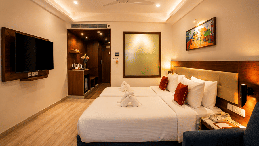 Deluxe Twin Room with Balcony at Sobit Sarovar Portico, Goa offering twin beds, contemporary interiors, private balcony, flat-screen TV, minibar, seating area and thoughtful amenities for a relaxing stay.