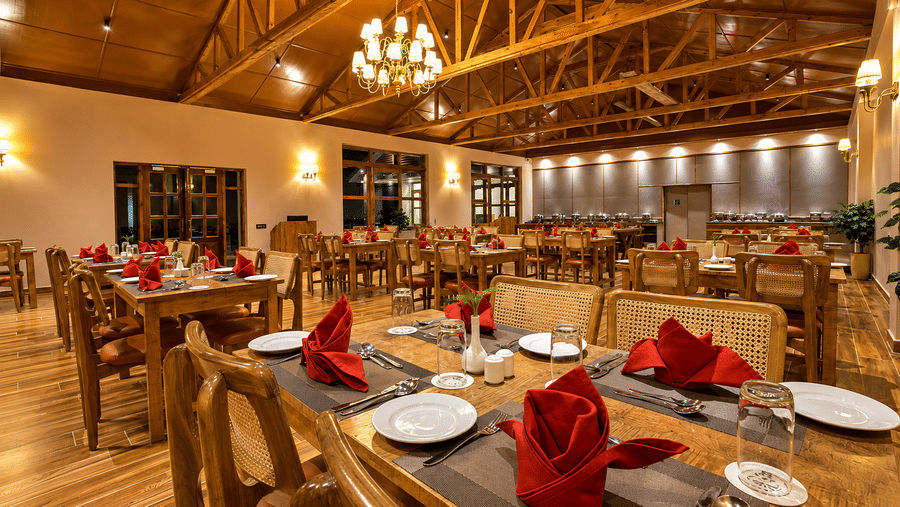 The dining room at Summit Rungkhung Village Resort - The Signature Collection shows wooden tables set with plates and folded napkins, wooden chairs, chandeliers, wall lamps and exposed ceiling rafters.