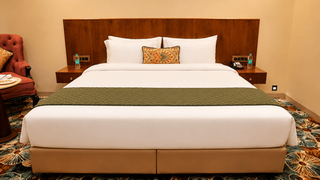 Double bed with a wooden headboard, green bed runner, and a floral carpet at Kadamb Kuteer, Vrindavan.
