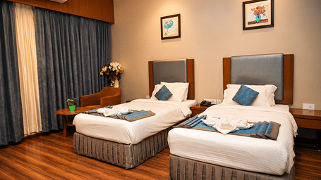 Club Superior Room with twin beds, blue accents, and floral decor at Pipul Padmaja Premium Hotel, offering a bright and cozy stay.