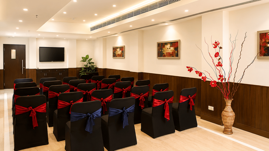 Conference room set up theatre-style with rows of black chair covers and blue sashes, framed artwork and a floral display in the corner.