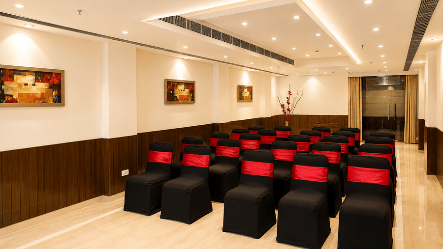 Conference room set up theatre-style with rows of black chair covers and red sashes, framed artwork and warm ambient ceiling lighting.