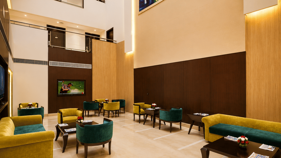 Hotel lobby lounge with teal and yellow armchairs, framed wall art, warm lighting and polished tiled flooring spread throughout the space.
