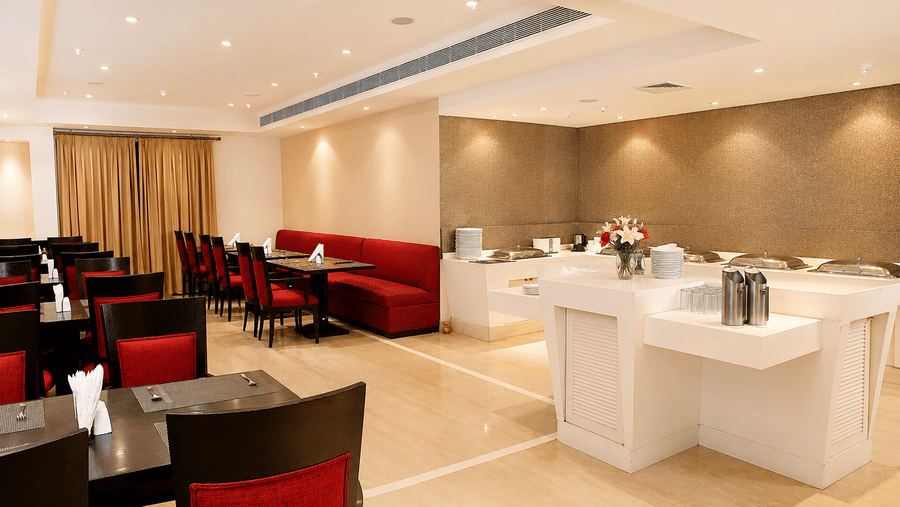 Restaurant dining area with red chairs and booth seating, a buffet counter and recessed ceiling lighting spread throughout the space.