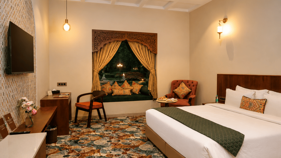 Guest room with a double bed, wall-mounted television, and warm wall sconce lighting at Kadamb Kuteer, Vrindavan.