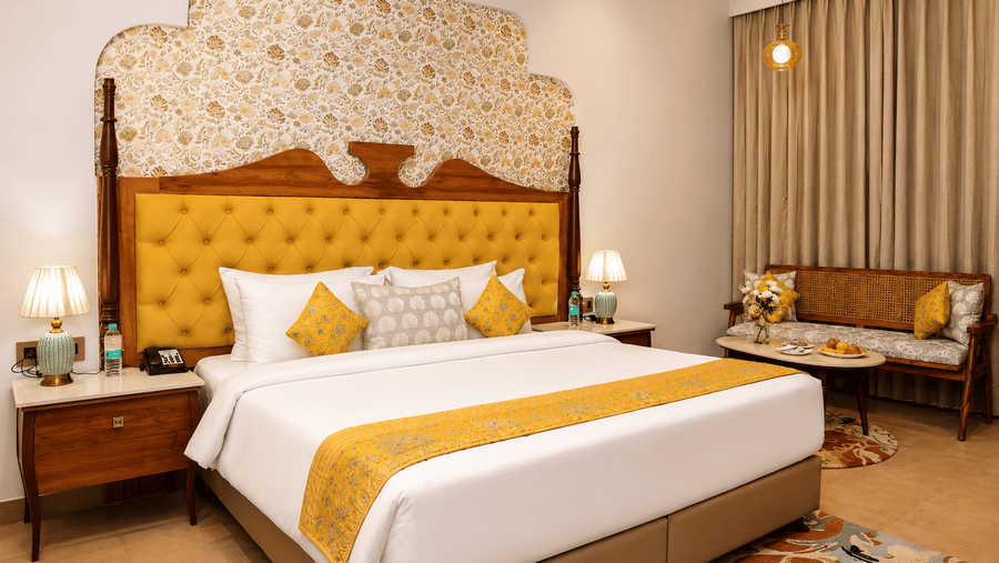 Guest room with a golden tufted headboard, double bed, white bedding, and yellow cushions at Kadamb Kuteer, Vrindavan.