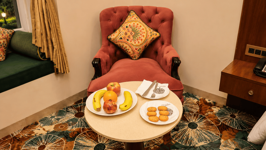 Room sitting area with a pink armchair, a small round table with fruit, and colourful upholstery at Kadamb Kuteer, Vrindavan.