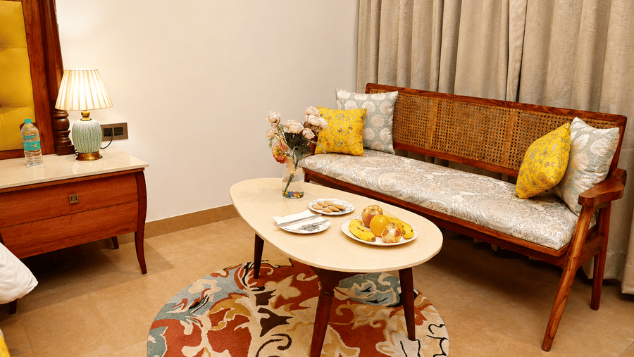 Room sitting area with a sofa, coffee table, yellow cushions, and a fruit platter at Kadamb Kuteer, Vrindavan.