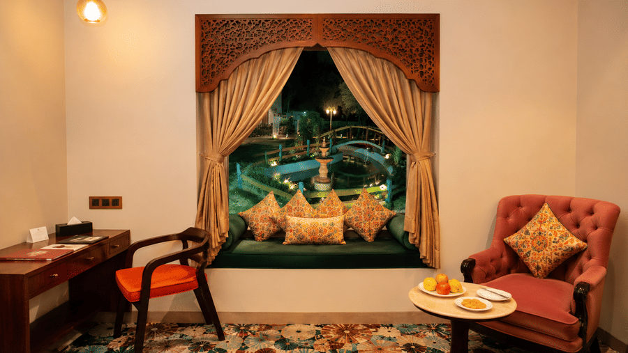 Guest room sitting area with a red armchair, side table, and a decorative wall mural at Kadamb Kuteer, Vrindavan.